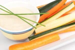 Fresh vegetable sticks with creamy dipping sauce on white plate