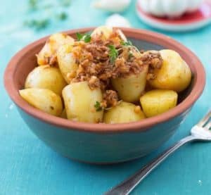 Bowl of roasted baby potatoes garnished with herbs and onions