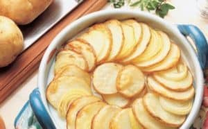 Baked scalloped potatoes in blue ceramic dish with herbs