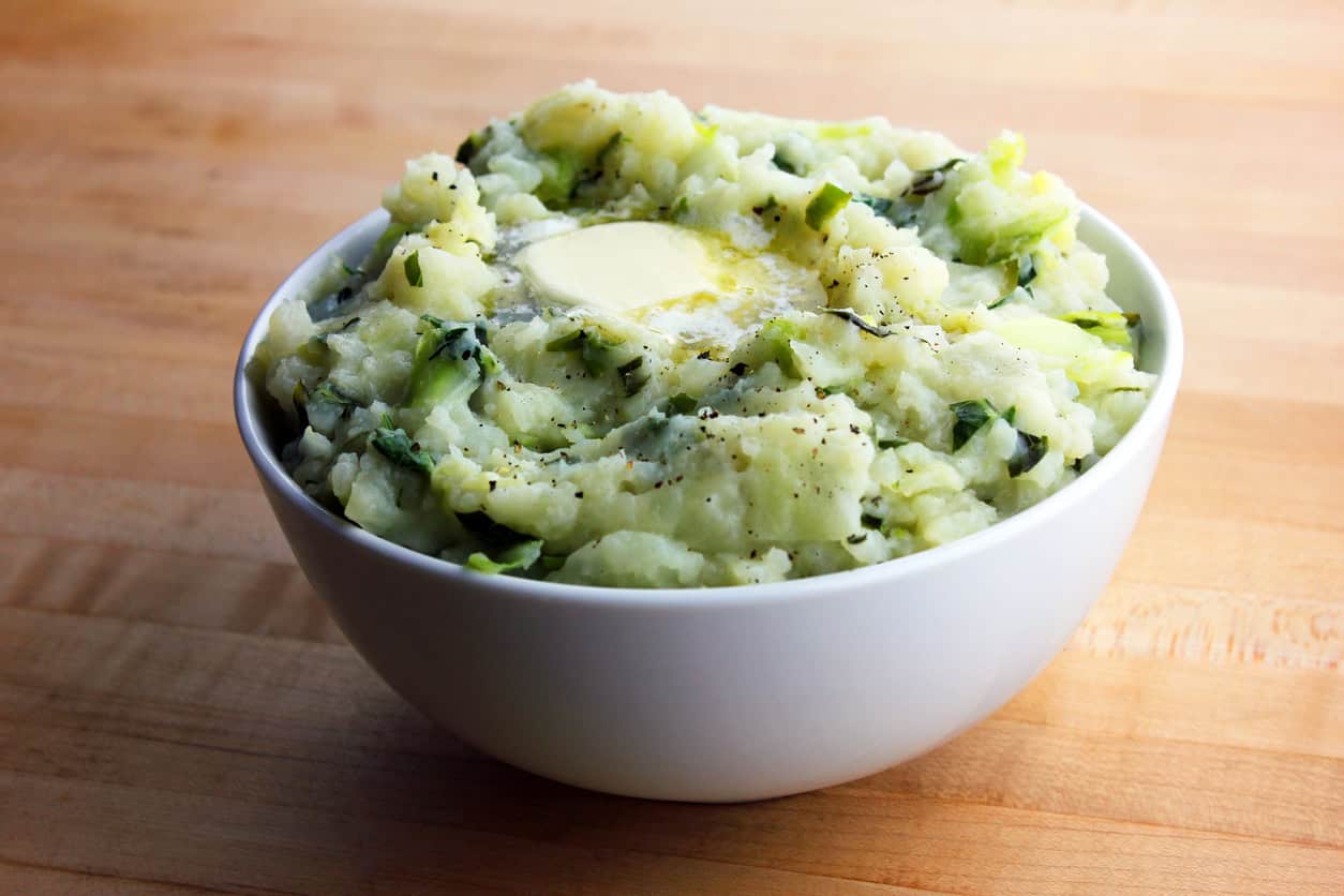 Bowl of mashed potatoes with butter and herbs on wooden table