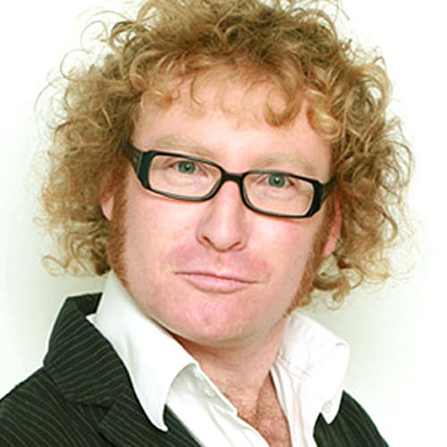 Man with curly red hair and glasses wearing suit jacket