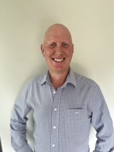Smiling bald man in checkered shirt standing against wall