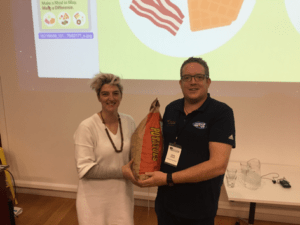 Two people holding a large red chili pepper prop indoors