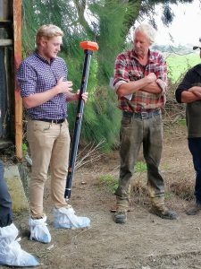 Man demonstrating agricultural tool to farmers outdoors.