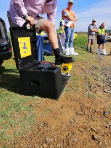 Person cleaning boots on boot scrubber machine outdoors with others watching