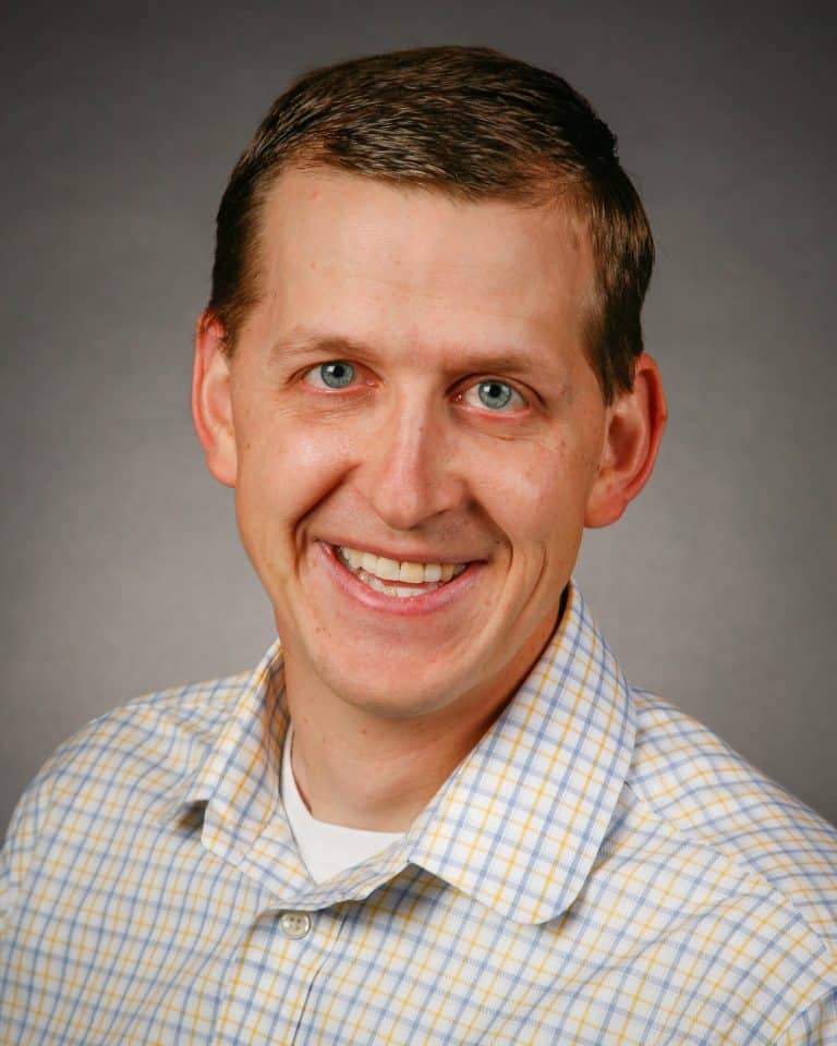 Smiling man with short brown hair wearing checkered shirt