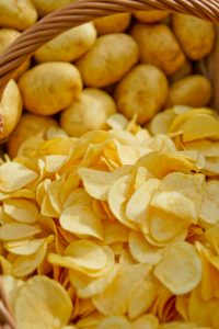 Basket filled with fresh potatoes and potato chips close-up