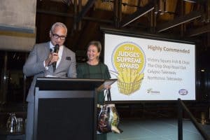 Man and woman presenting Judges' Supreme Award at ceremony.