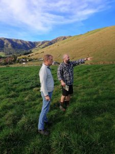 Two men standing and discussing on grassy hill under blue sky