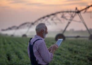 Senior farmer holding tablet in front of irrigation system in soybean field