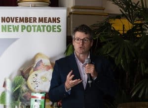 Man speaking with microphone near November means new potatoes banner