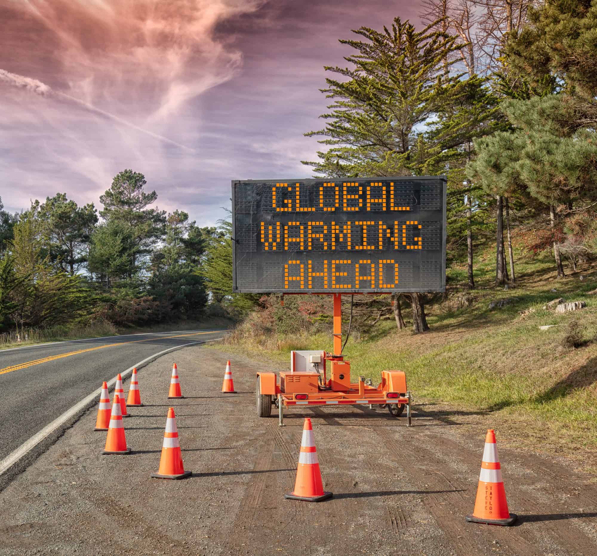 Global Warming AHEAD: This is a photograph of a mobile roadside sign parked on highway one in northern California. It is a trailer and powered by batteries and provides information and warnings for drivers by displaying words on a large panel display.