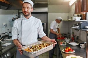 Smiling caucasian cook wearing uniform is doing his job. He prepares the necessary ingredients for his signature dish. Front view. Cooking concept