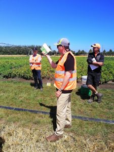 Farm workers in orange safety vests discussing crop field conditions