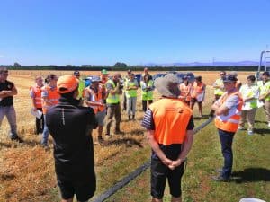 Group of people wearing safety vests in outdoor agricultural field meeting