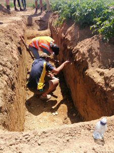 Two men inspecting soil layers in a deep excavation trench outdoors