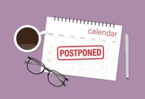 Calendar with "POSTPONED" stamp, coffee, glasses, pen.