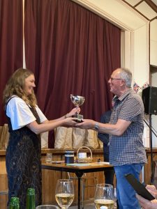 Man presenting trophy to smiling woman at indoor event ceremony.
