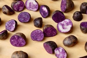 Purple potatoes sliced and whole on wooden surface background