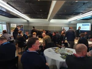 Business conference attendees seated around tables in meeting room