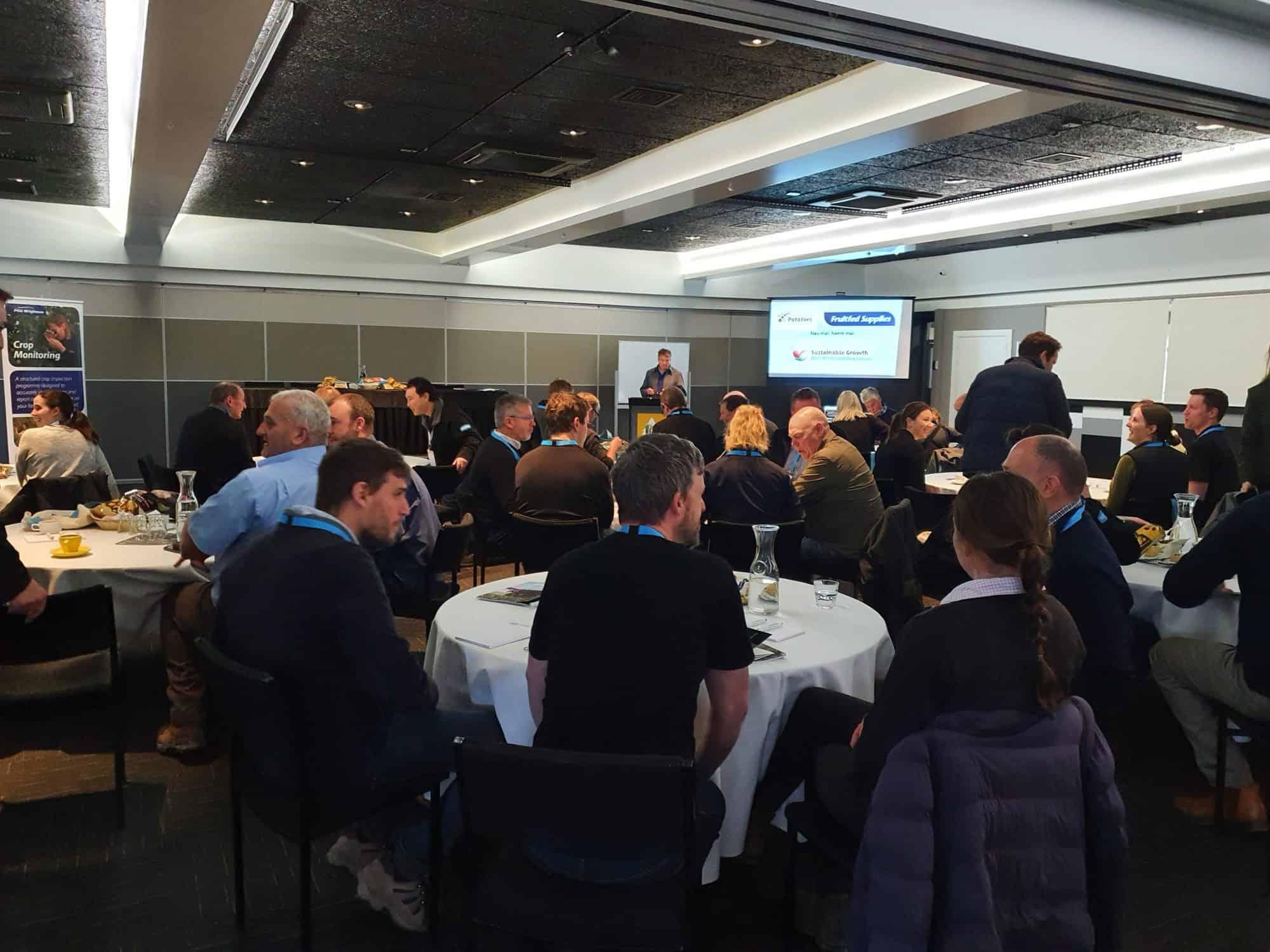 Business conference attendees seated at round tables listening to speaker