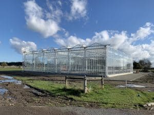 Large modern glass greenhouse structure under blue sky outdoors.
