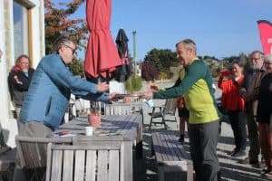 Two men exchanging an award outdoors with people watching.