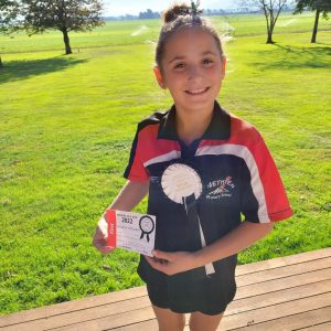 Young girl holding award certificate and ribbon outdoors