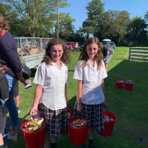 Two schoolgirls in uniforms carrying red buckets outdoors