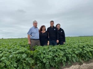 Four people standing in green potato farm field under cloudy sky