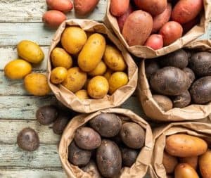 Assorted colorful potatoes in paper bags on wooden table