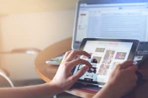 Hands using tablet for browsing photos with laptop in background