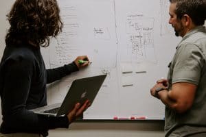 Two men brainstorming website design on whiteboard with laptop