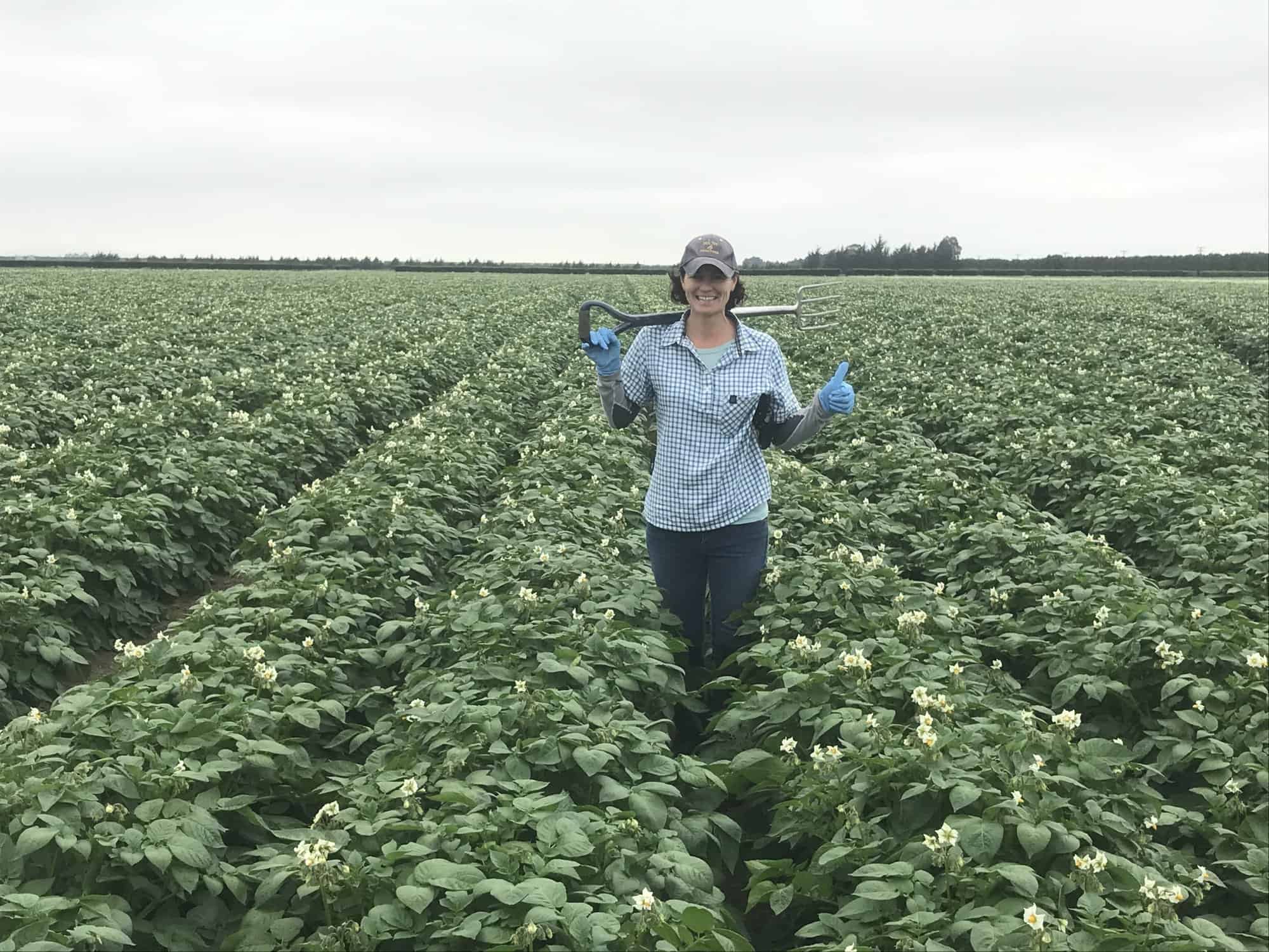 Woman in plaid shirt holding garden fork in potato field