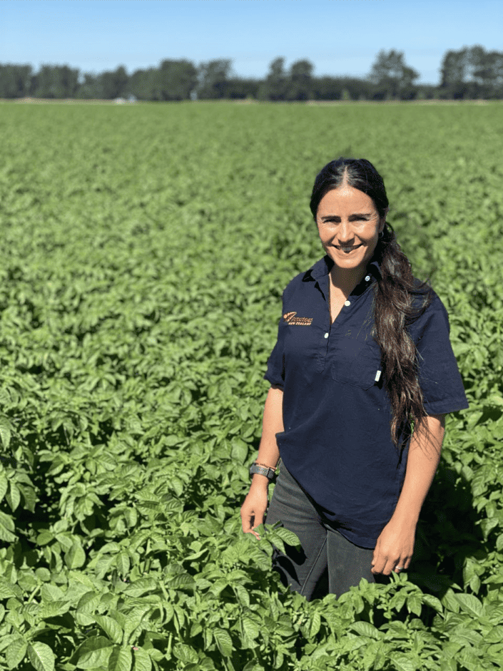 Woman standing in green agricultural field under clear blue sky
