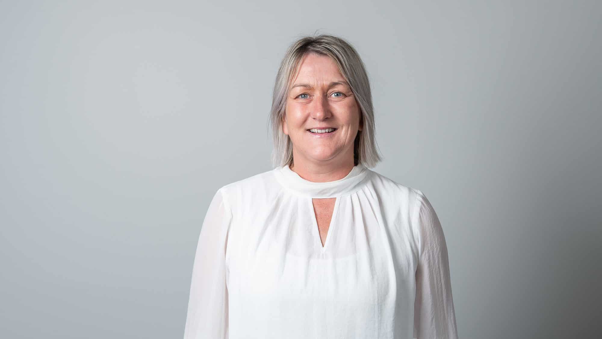 Smiling middle-aged woman wearing white blouse on gray background