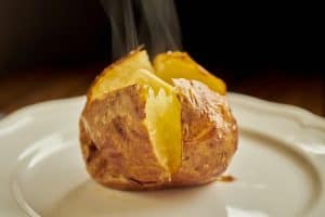 Baked Potato sliced open filled with melting butter on a white plate.