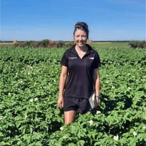Woman standing in green field holding notebook under clear blue sky