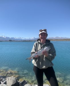 Woman holding fish by clear blue lake with snowy mountains background