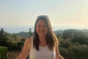 Smiling woman in white top outdoors with sunny landscape background
