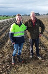 Two male farmers standing in a harvested field under cloudy sky
