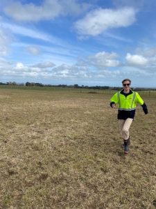 Person walking in bright jacket across open grassy field under blue sky