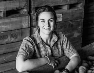Smiling woman in plaid shirt with crate of potatoes black and white