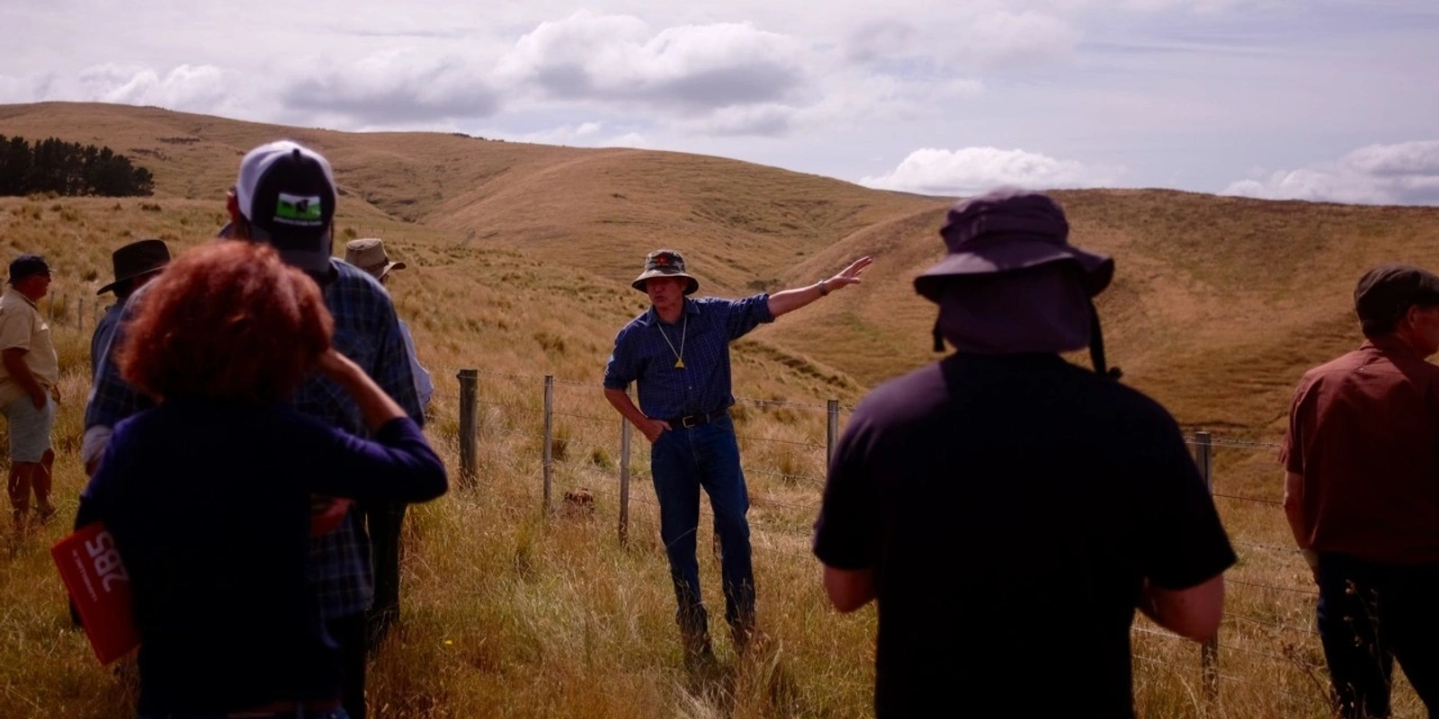Group of people listening to a guide in grassy hills outdoors.