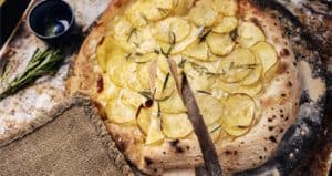 Thin-crust potato rosemary pizza on rustic wooden surface