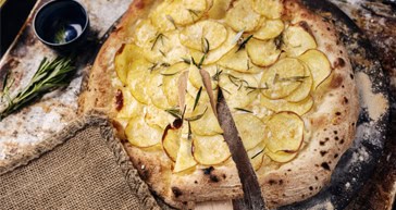 Thin-crust potato rosemary pizza on rustic wooden surface