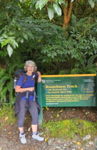 Woman hiker standing next to Routeburn Track sign in forest