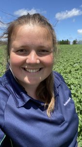 Smiling woman in blue shirt standing in green field outdoors