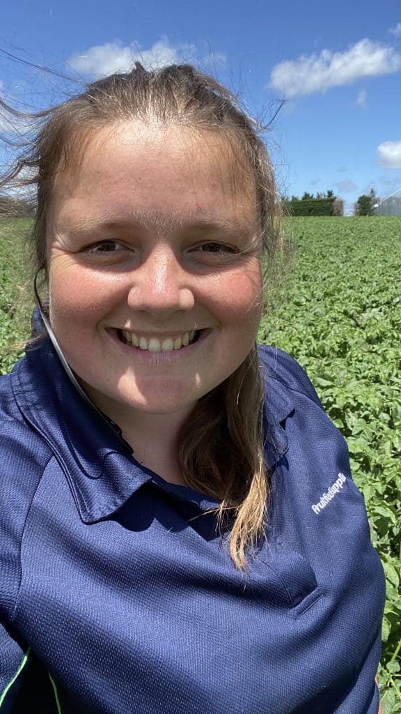 Smiling woman in blue shirt standing in green field outdoors