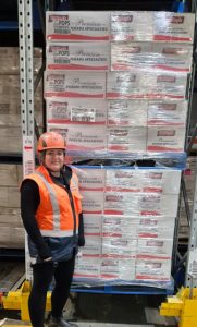 Warehouse worker wearing safety gear standing by stacked potato boxes